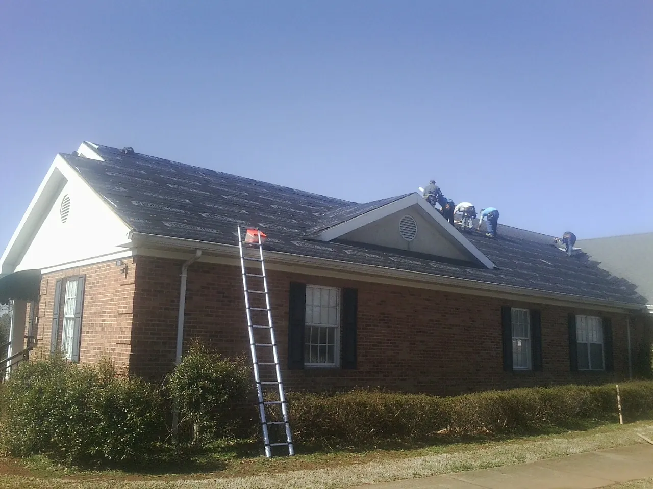 Crew tearing shingles off a brick ranch roof with a ladder set — Emergency Roof Repair work by our crew in Bearsville