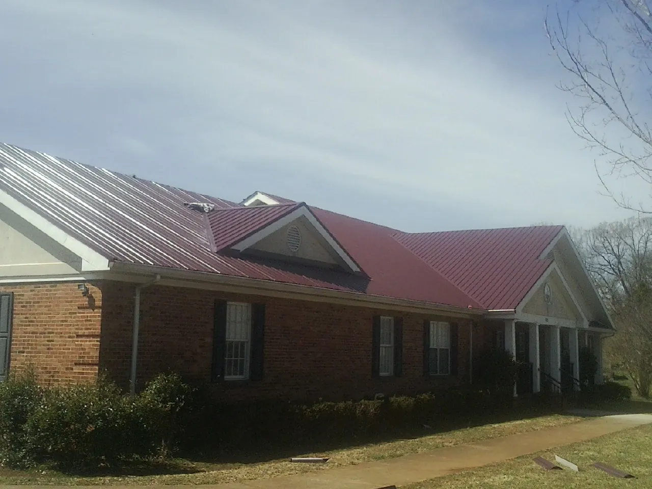 Red metal roof with gabled entries on a long brick building, from a Hail Damage Roof Repair job in Bearsville