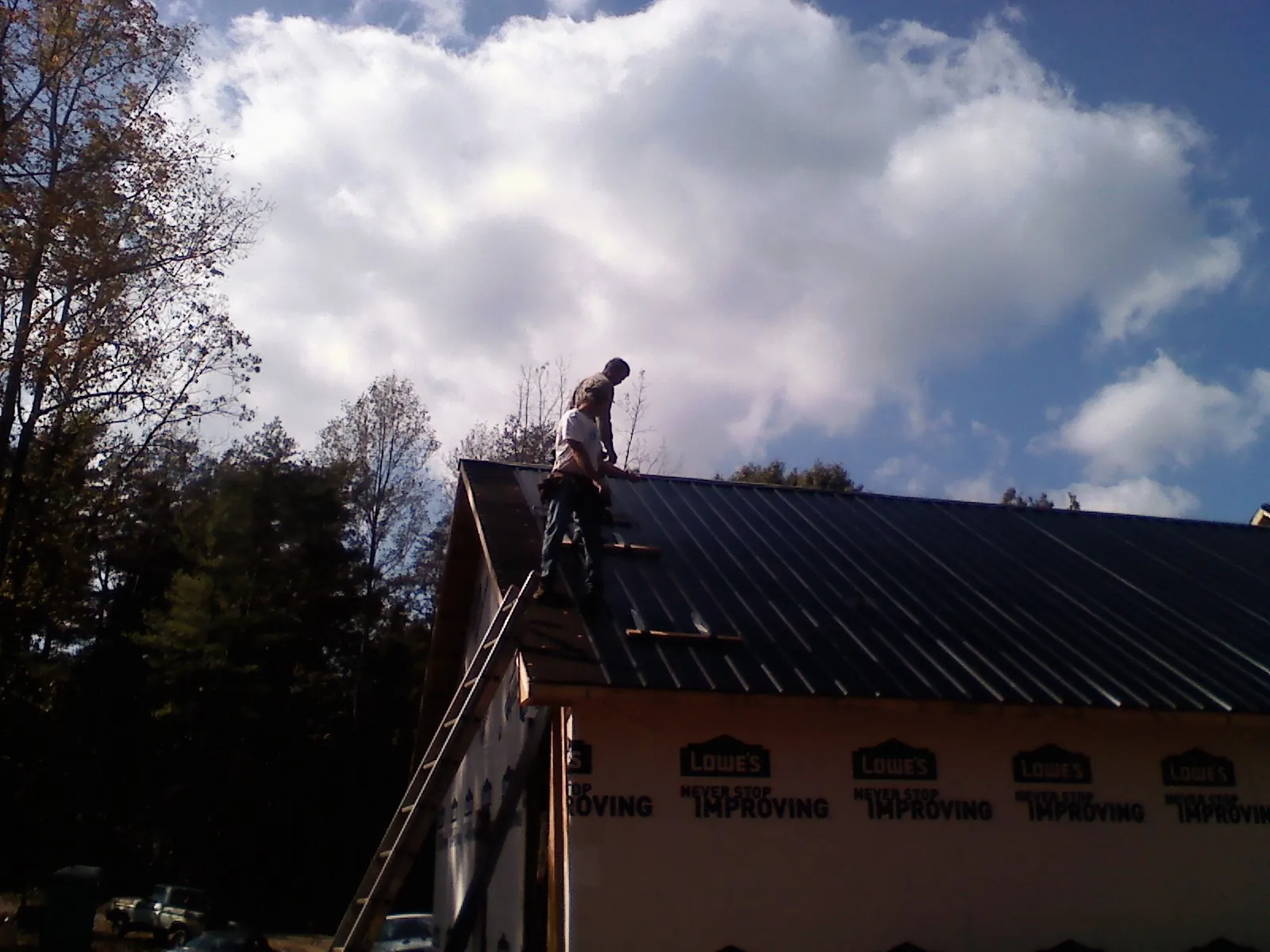 Roofer fastening dark metal panels high against a cloudy sky, from a Roof Inspection job in Bearsville