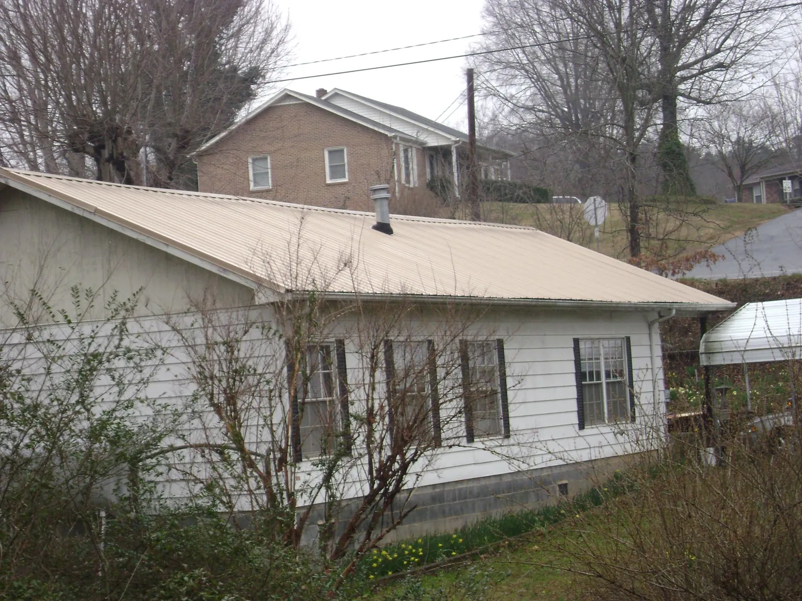 Tan metal roof on a white sided house set into a hillside — Commercial Roofing by Roofing Brothers in Bearsville